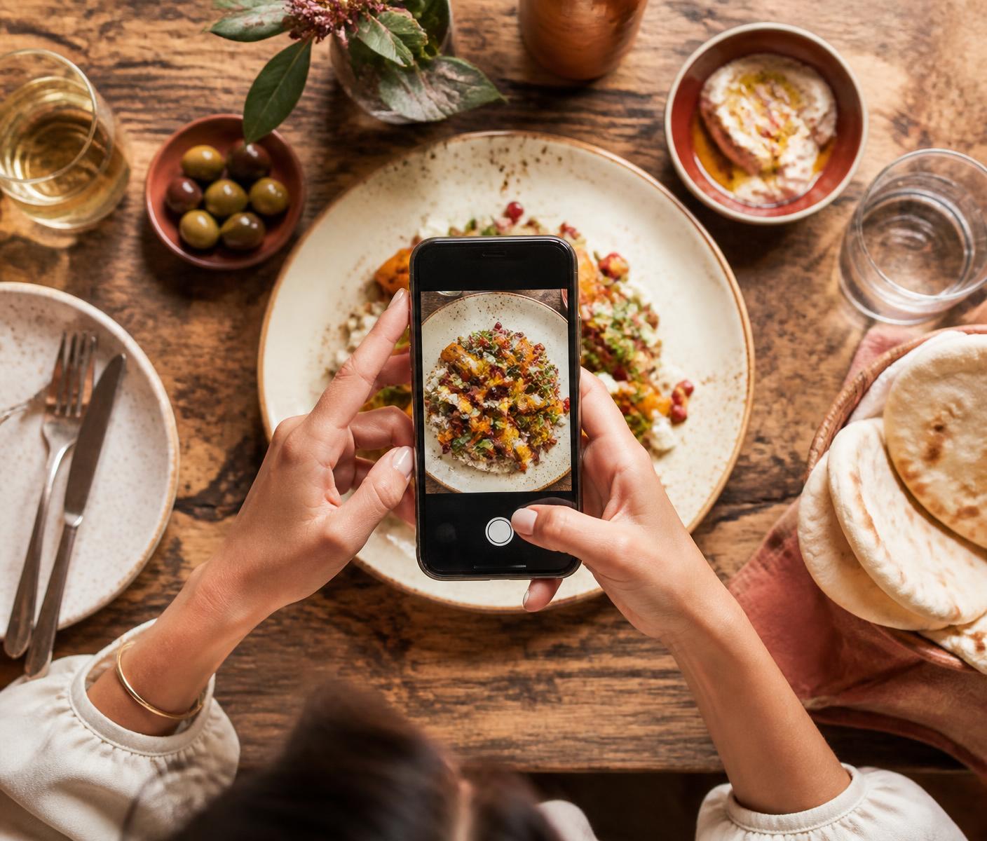 Persona filmando con el celular un plato servido en una mesa de restaurante